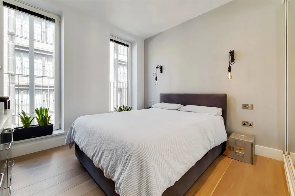 Double bedroom with tall windows, wall lights and fitted wardrobes