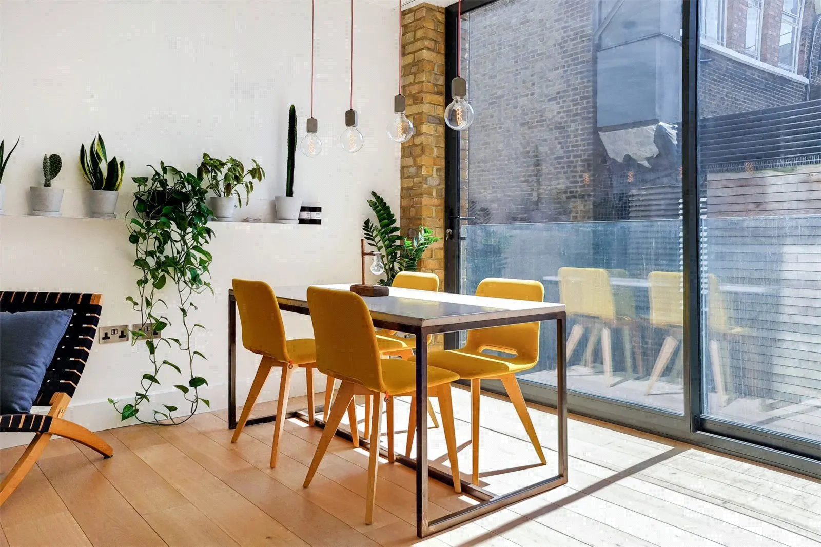 Sunlit dining area with plants beside floor-to-ceiling glazing