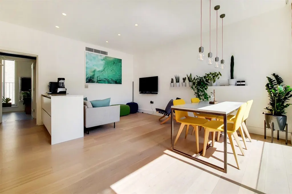 Sunlit open-plan living and dining room with oak floors and yellow chairs